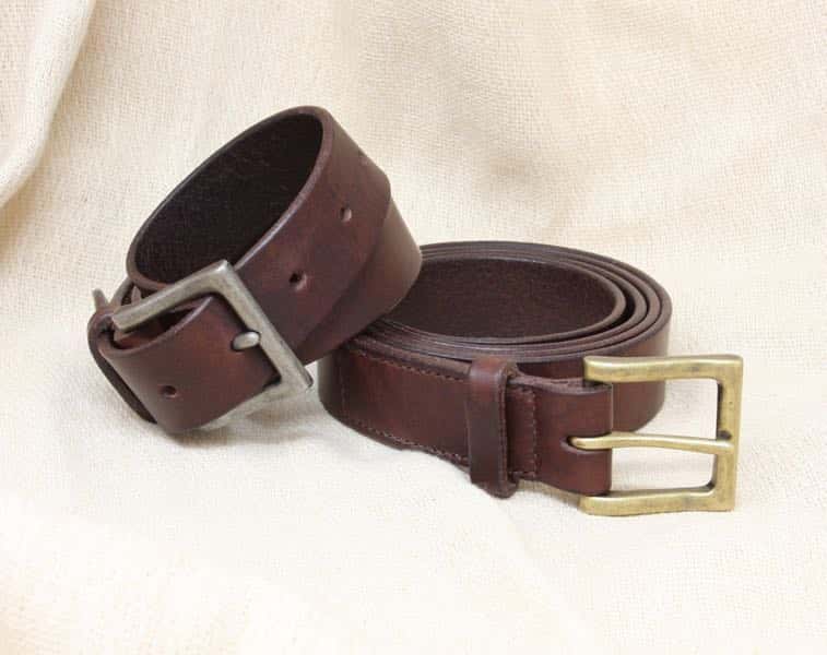 Italian leather belts against canvas background. One with antique nickel buckle and one with antique brass buckle