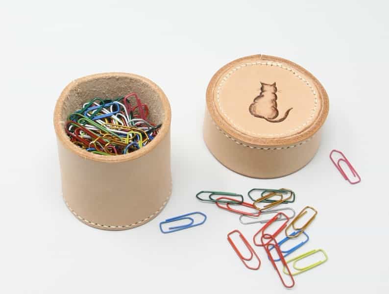 Small round leather box with cat motive, shown holding paper clips