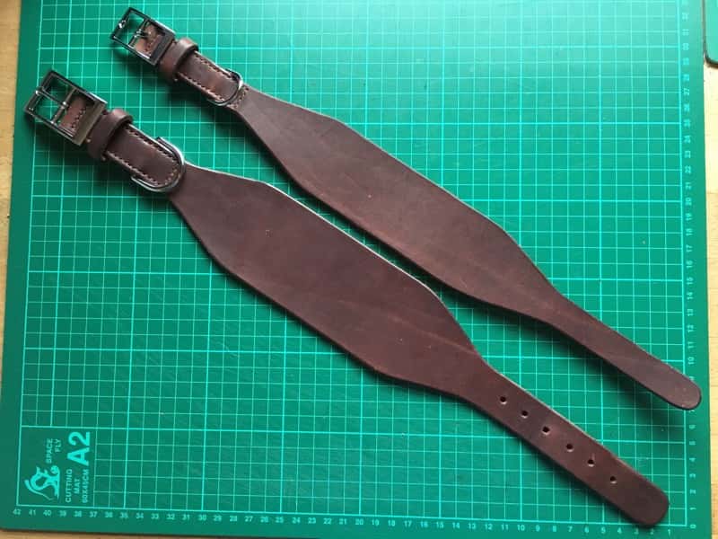 Large and small italian brown leather greyhound collars laid flat on cutting board.