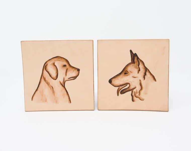 Pair of dog head motif square leather drinks coasters on a white background