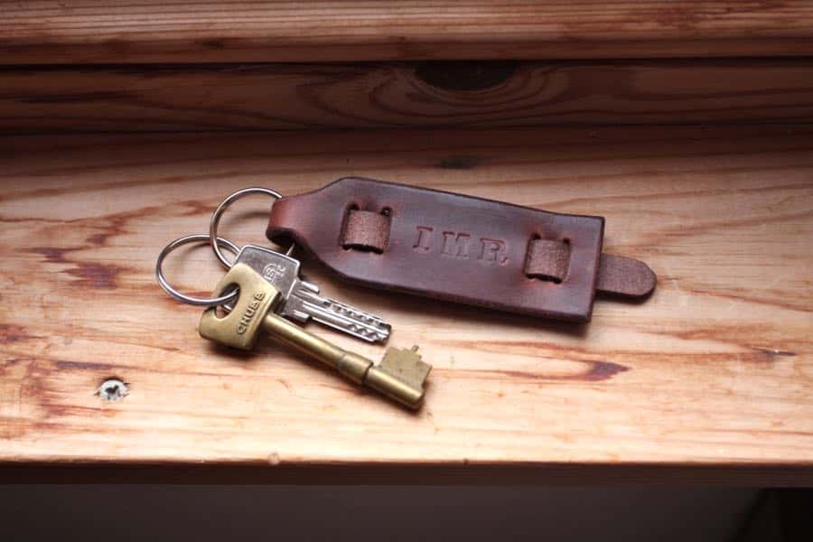 Brown leather personalised key fob / key ring on a wooden window sill.