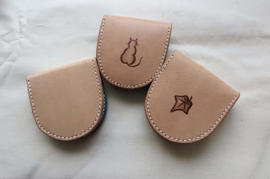 Back of three small leather coin pouches showing plain, cat and leaf motifs