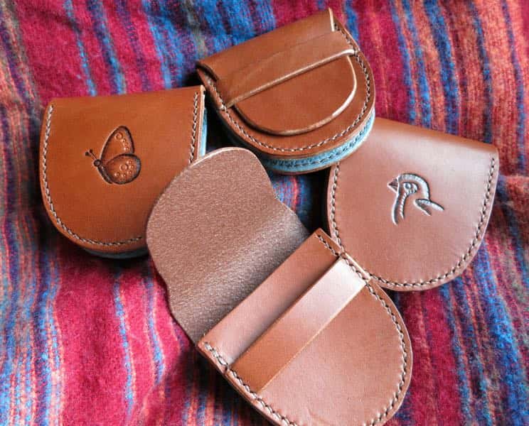 Four small brown leather coind pouches showing plain, butterfly and bird motifs