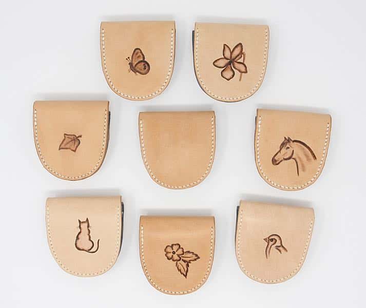 Backs of small leather coin pouches showing horse, cat, flower, bird, butterfly and ivy leaf motifs