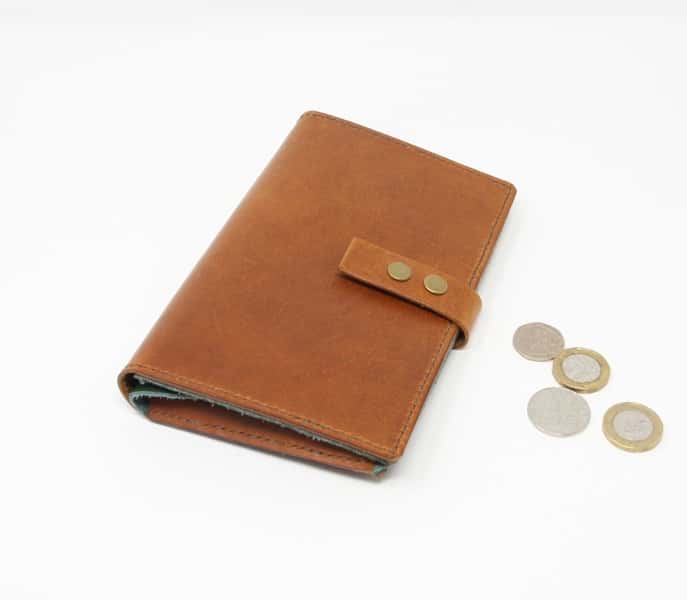 Tan leather wallet style purse with green interior shown closed with pound coins for scale