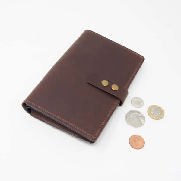 Dark brown leather wallet style purse with navy blue interior shown closed with pound coins for scale