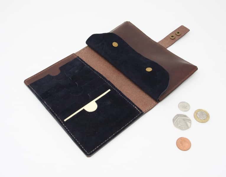 Dark brown leather wallet style purse with navy blue interior shown open with pound coins for scale